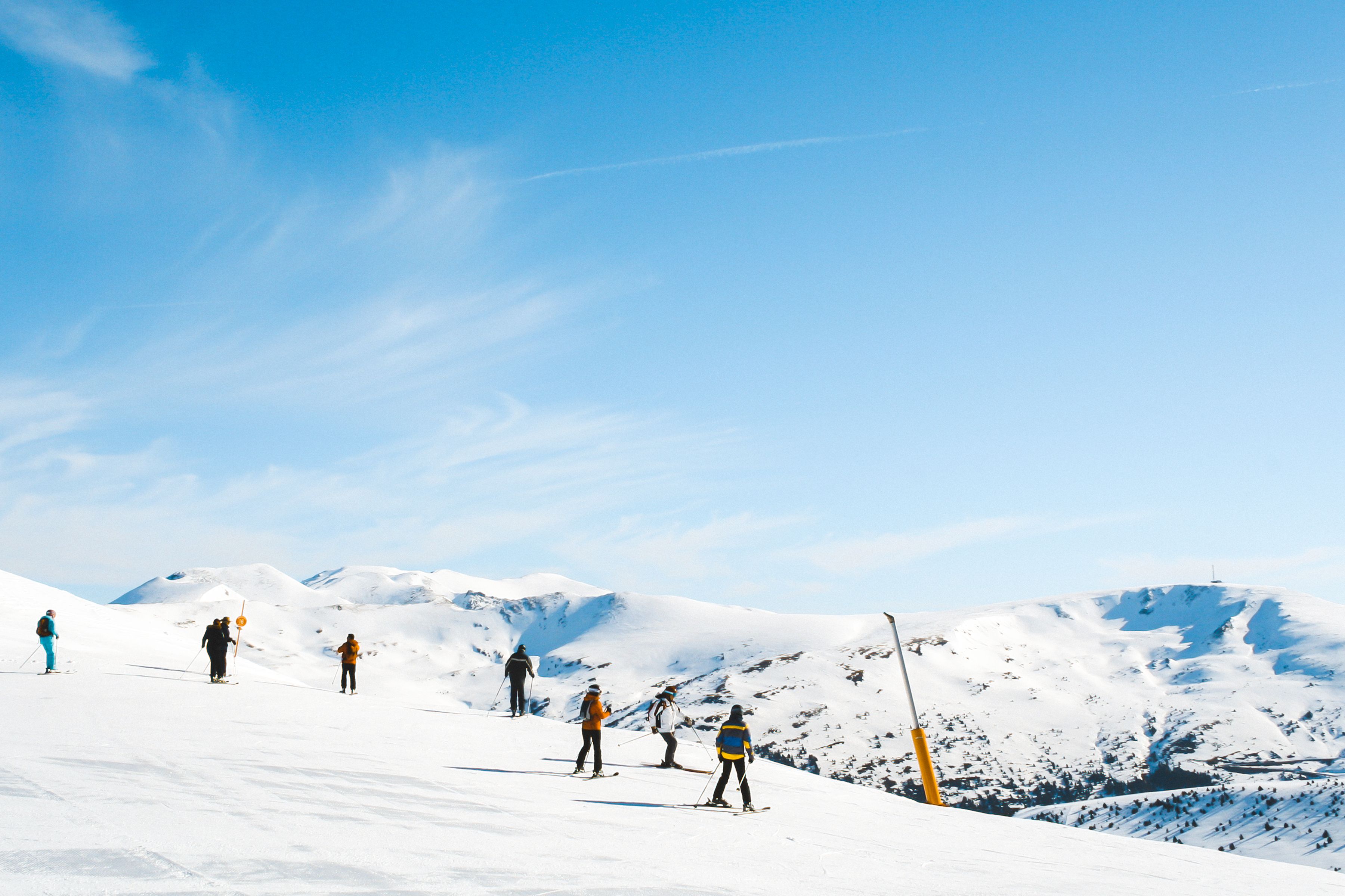 Skiers enjoying an open snowy mountain beneath a blue sky